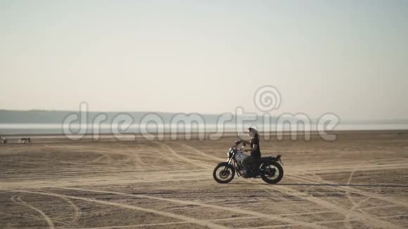 美丽的年轻女子骑着一辆旧摩托车玩着诡计在日落或日出的沙漠里女司机稳定的视频的预览图