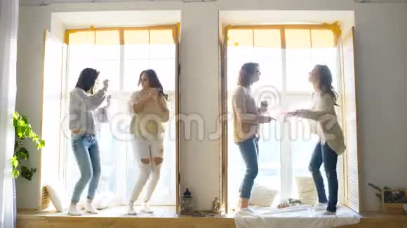 快乐和美丽的女朋友在窗户上跳舞在卧室里玩得开心和快乐视频的预览图