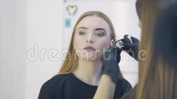 发型师在美容院为卷发美女修眉用天然染料染眉视频的预览图