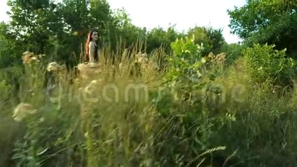 幸运的黑发少女穿着黑色衣服在草地和树木之间的绿色田野上行走视频的预览图