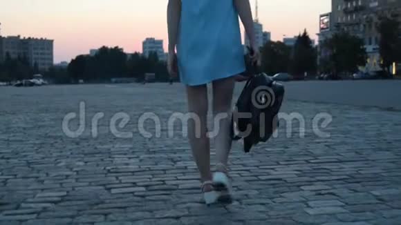 傍晚穿着一件连衣裙背着背包走在街上的年轻苗条的女孩视频的预览图