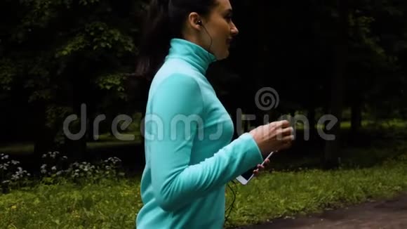 快乐运动的女人戴着耳机在公园柏油路跑步视频的预览图