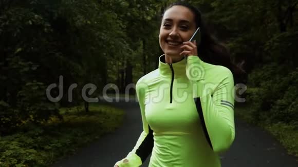 漂亮的运动女人在公园里用智能手机慢跑和跑步视频的预览图