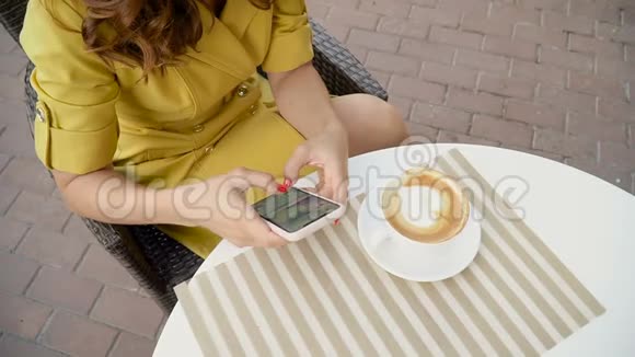 穿黄色衣服的女孩在咖啡馆的露台上使用智能手机视频的预览图