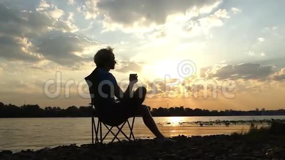 年轻人在夕阳下的河岸边吃想喝咖啡视频的预览图