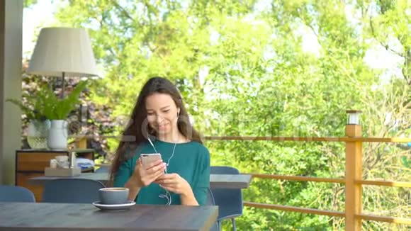 年轻女子带着智能手机在温暖的白天独自坐在咖啡店里可爱的女性可爱的微笑视频的预览图