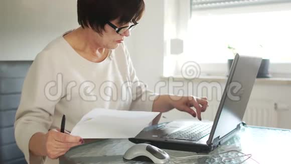 一个穿着商务服和眼镜的女人正在用她的笔记本电脑工作附近有纸账愿意考虑视频的预览图