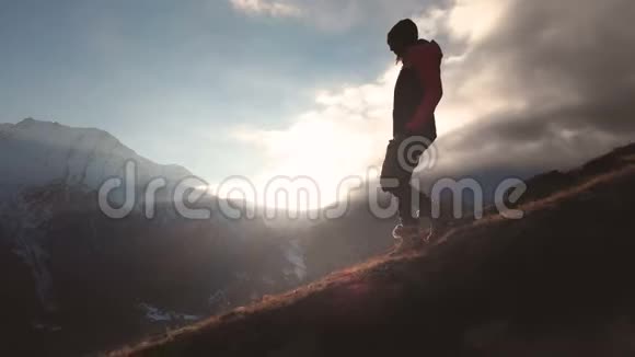 在美丽的日落中一个女孩走在山的边缘作为一个剪影的史诗镜头的长镜头鸟瞰视频的预览图
