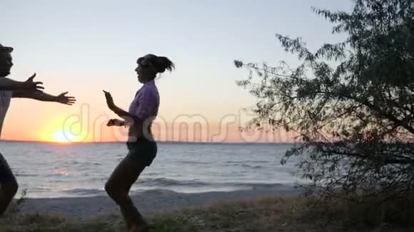 女孩在日落时分跳到岸边的河边夕阳西下的幸福情人在海边拥抱年轻的夫妇视频的预览图