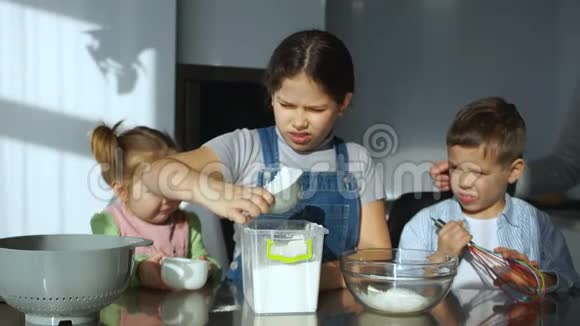 三个漂亮的孩子在厨房里做饭把鸡蛋打碎成面粉倒水揉面视频的预览图