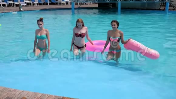 穿泳衣的女孩子从泳池边出来戴着鲜艳的粉红色橡胶圈穿着比基尼的漂亮年轻女性休息视频的预览图