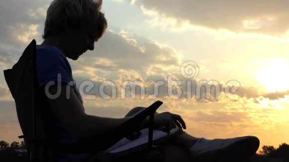 智能博客坐在折叠椅上看着日落时的平板电脑视频的预览图
