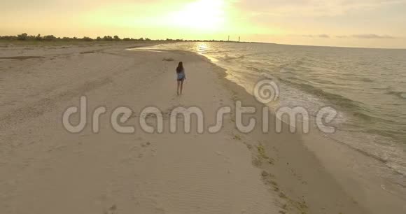空中美丽的女孩在日落时沿着沙滩漫步视频的预览图