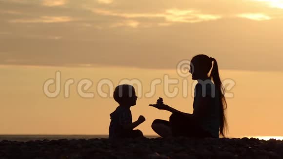 妈妈和儿子在海滩上玩石头日落时间剪影视频的预览图