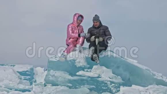 在冰封的湖面上年轻夫妇在冬天散步时玩得很开心情侣们坐在蓝色的大冰块上视频的预览图