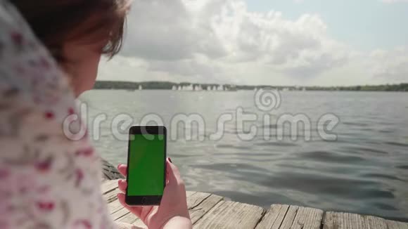女孩躺在河边的木墩上看着绿色的智能手机屏幕滚动它视频的预览图