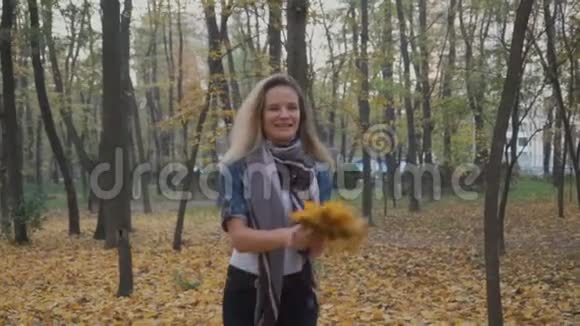 快乐的女人带着一束叶子走在秋天的公园里视频的预览图