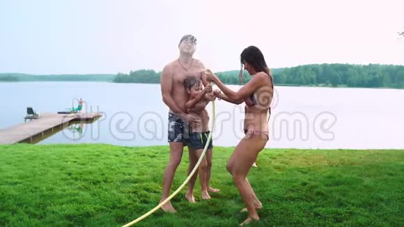 爸爸妈妈和两个儿子在夏天的草地上为草坪浇了一根水管在湖边的乡村别墅视频的预览图