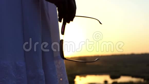一个年轻苗条的女人站在斯隆莫的夕阳下手里拿着太阳镜视频的预览图