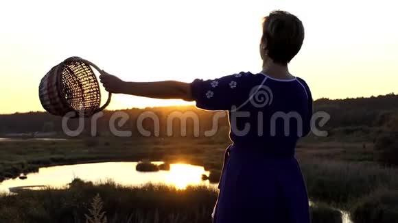 女人在日落时缓慢地摇动柳条篮子视频的预览图