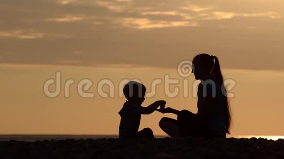 妈妈和儿子在海滩上玩石头日落时间剪影视频的预览图