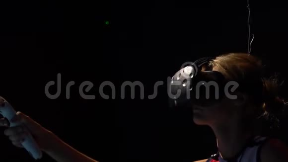 一个戴着虚拟现实眼镜的女孩在黑暗的房间里把她的手放在她手中的一侧她拿着一个快乐的东西视频的预览图