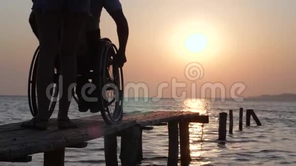 关心坐在轮椅上的人享受水面上美丽的日落视频的预览图
