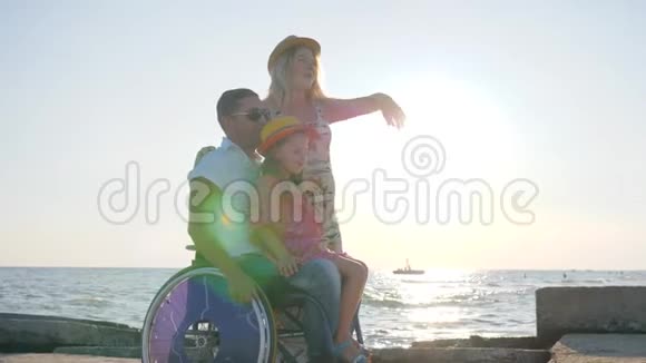 快乐的无效一家人一起在背景蓝天上玩耍女孩坐在轮椅上张开双臂视频的预览图
