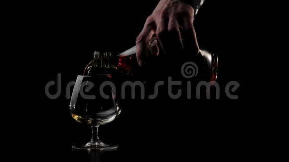 豪华白兰地手把一个圆瓶里的金白兰地倒进黑桌子上的一个杯子里背景是黑色的布兰迪视频的预览图