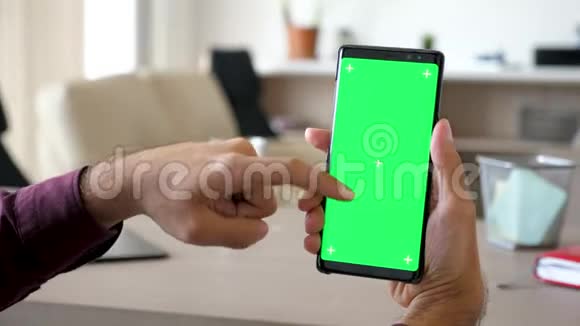 一个人在客厅里使用一款带有绿色屏幕色度模型的现代智能手机视频的预览图