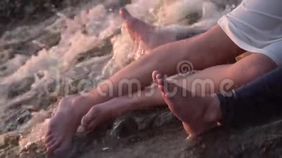一个穿牛仔裤的男人和一个穿白色连衣裙的女孩的腿躺在流动的水中的石头上的怀抱里视频的预览图