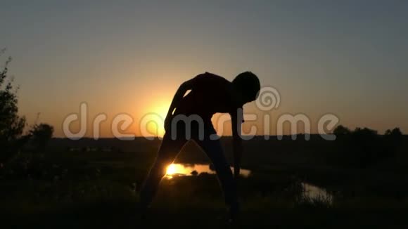 小男孩在日落时在湖岸慢动作做身体锻炼视频的预览图