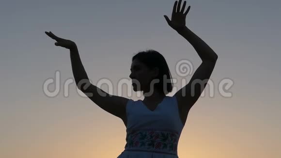 一个年轻苗条的女人在斯隆莫的夕阳下用双手跳舞视频的预览图