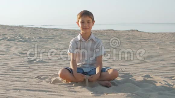 夏天穿着白色衬衫的可爱男孩坐在沙滩上大海背景下的肖像视频的预览图