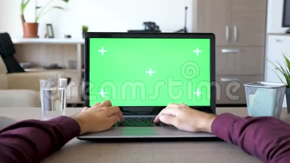 男性手在笔记本电脑上打字客厅里有一个模拟的绿色屏幕色度视频的预览图