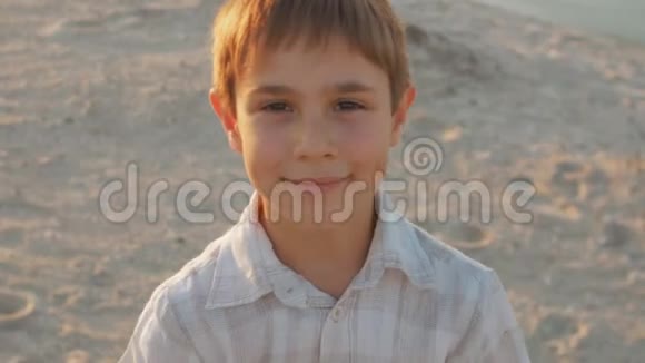 日落时分一个穿着白色衬衫的10岁男孩在夏日海滩上的肖像视频的预览图