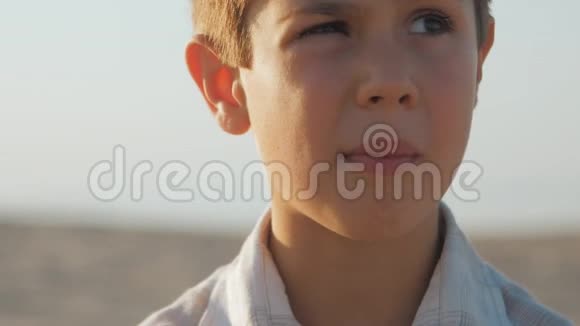 在沙滩上为一个穿着白色衬衫的小男孩特写肖像视频的预览图
