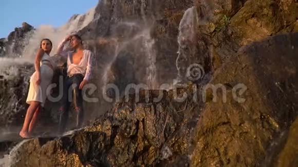男孩和女孩站在瀑布旁边看日落视频的预览图