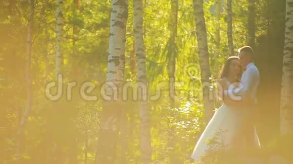 优雅幸福的新婚夫妇在日落时分在森林里接吻视频的预览图