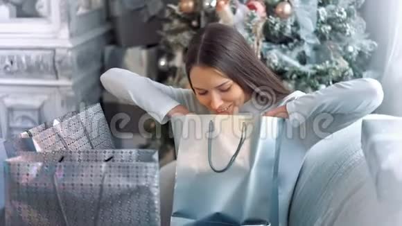 微笑着幸福的女人手里拿着圣诞礼物在圣诞树前视频的预览图