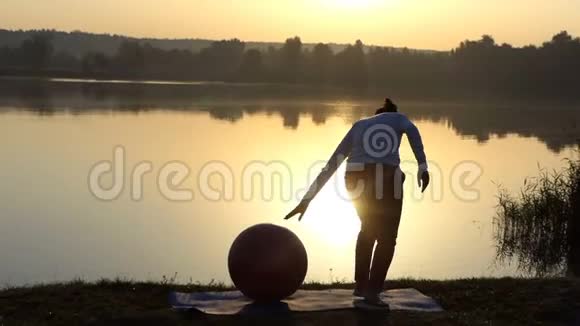 苗条的女人在日落时把手放在健身球上视频的预览图