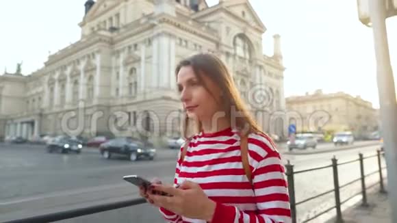 日落时分年轻女子用智能手机走在一条老街上通信社交网络网上购物视频的预览图