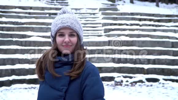 戴着冬帽的漂亮女人微笑着站在森林里的雪地上背景是雪楼梯一幅肖像画视频的预览图