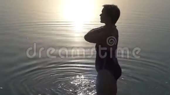 日落时分一个身穿泳装的女人站在湖边视频的预览图