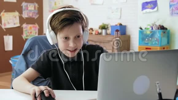 可爱的小男孩戴着耳机在笔记本电脑上玩电脑游戏视频的预览图