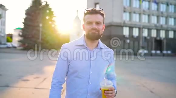 男人在智能手机上说话喝着果汁沿着街走慢动作视频的预览图