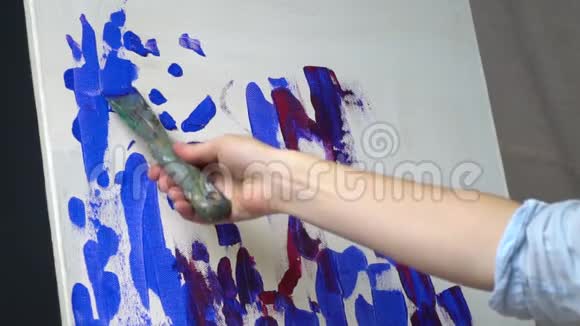 女性用涂抹在颜料中的手慢慢地用铲子涂抹在画布上视频的预览图