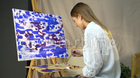 布鲁内特画家坐在画布前将油画颜料混合在木制调色板上视频的预览图