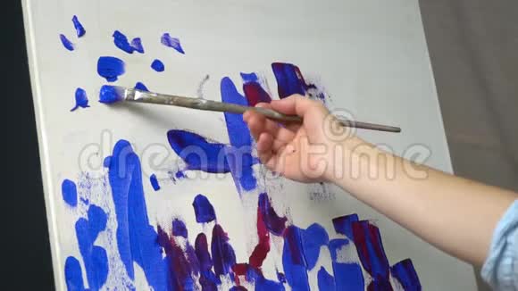 涂在颜料上的女性手在画布上刷上蓝色的笔视频的预览图