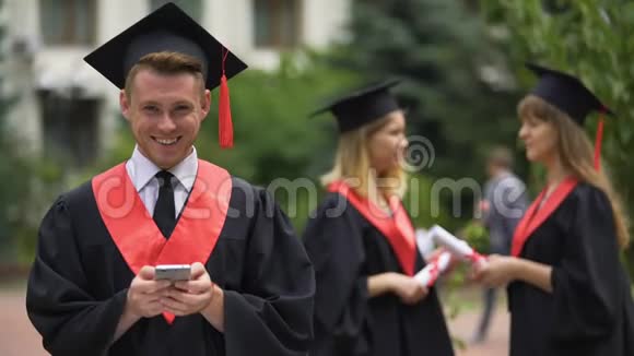 微笑男毕业生拿着智能手机看着镜头毕业视频的预览图